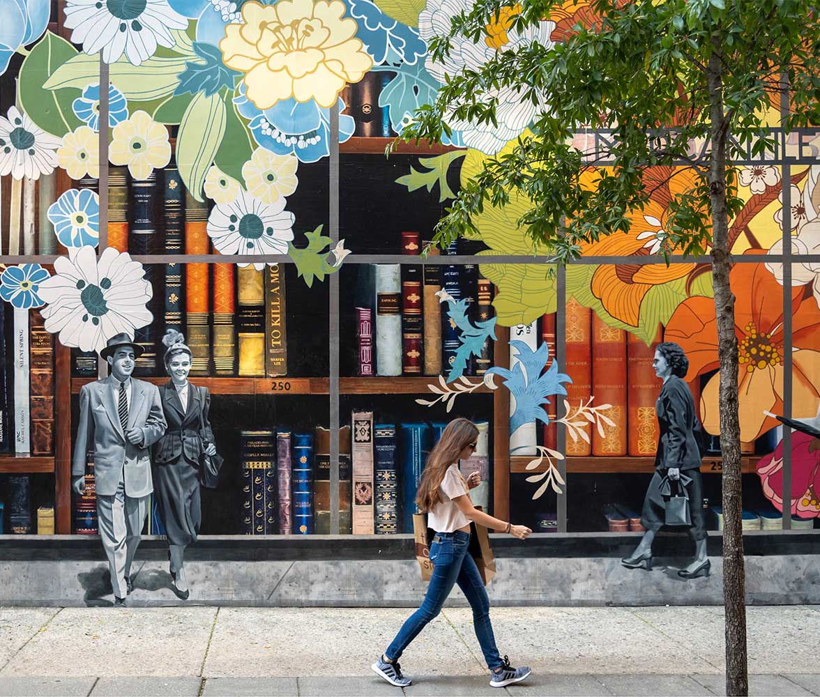 Person walking past storefront with painted book mural.