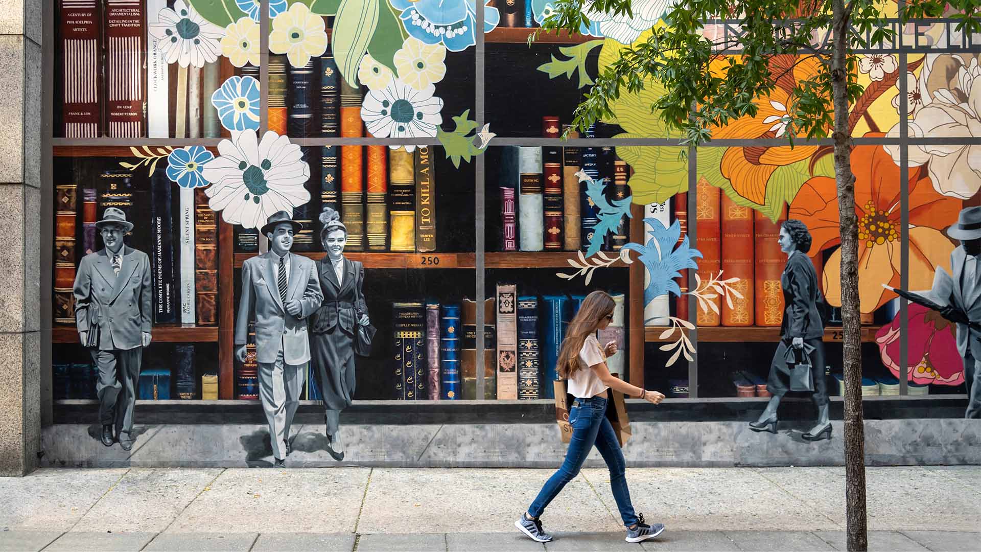 Person walking past storefront with painted book mural.